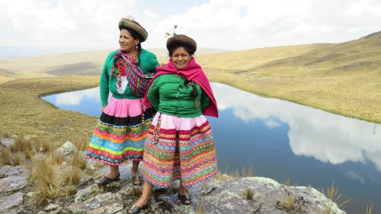 Zwei Frauen stehen vor Teich mit auffälliger traditioneller Bekleidung