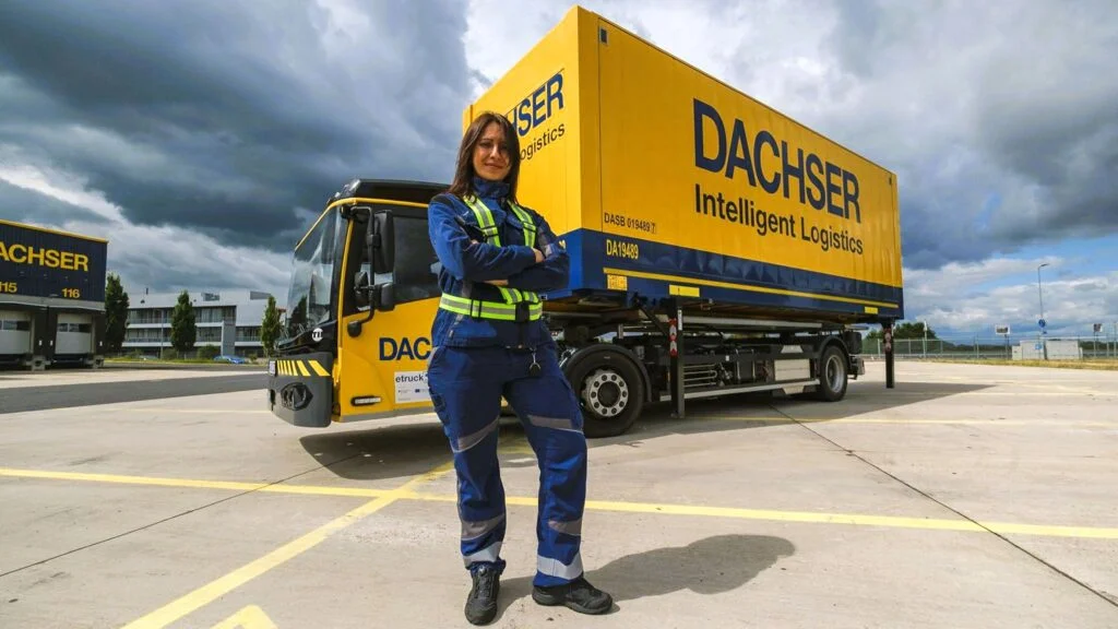 Eine Mitarbeiterin von DACHSER Erlensee steht vor eine Hoffahrzeug mit elektrischem Antrieb, auch E-Wiesel genannt, beladen mit einer Wechselbrücke.