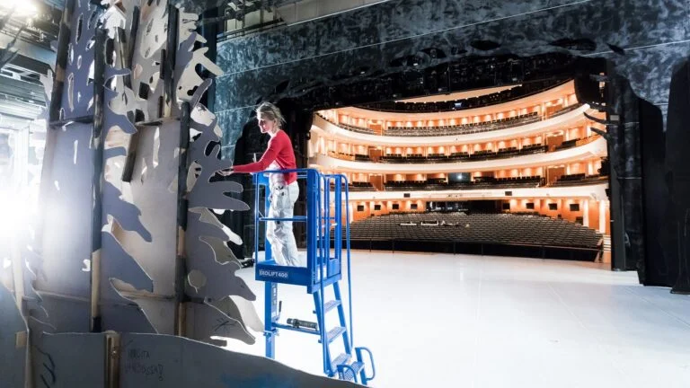 Person arbeitet auf kompakter Ixolift-Arbeitsbühne auf einer Theaterbühne vor Zuschauerrängen – sicheres Arbeiten mit ergonomischer Hebetechnik als Alternative zu Leiter